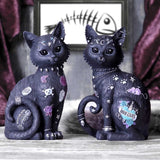 Two decorative cat figurines with tattoos and jewelry on a wooden surface.