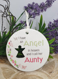 Round white plaque with text and an angel silhouette, surrounded by purple flowers and greenery.
