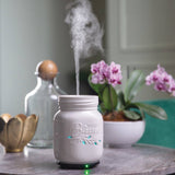 White mason jar-shaped diffuser emitting steam on a table with decorative items.