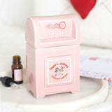 Pink mailbox-shaped container with 'Mail' text, next to a small bottle and dropper on a white surface.
