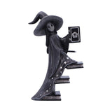 Statue of a witch with a black hat and long coat, holding a book and pentacle symbol on a white background.