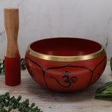 Red singing bowl with gold rim and OM symbol on a wooden surface with a white marble background