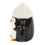 Black mug with a penguin design and a white knit lid on a white background
