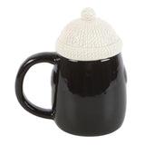 Black mug with a white knit beanie on a white background