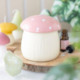 Mushroom-shaped oil burner on a wooden surface with candles and essential oils in the background
