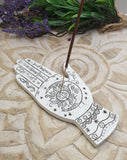 Decorative hand-shaped incense holder with sun design on a stone surface with lavender.