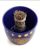 Blue cup with gold polka dots containing a sage bundle on a white background