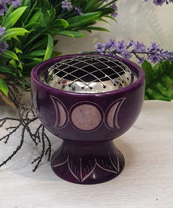 Purple decorative item with silver top on a white surface with green and purple plants in the background