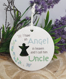 Round ceramic ornament with text and silhouette of a person, surrounded by greenery and purple flowers.