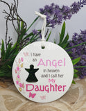 Round ceramic ornament with text and silhouette of a person, set against a floral background.