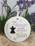 Round ceramic tag with text and silhouette of a person, surrounded by greenery and purple flowers.