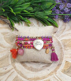 Set of colorful beaded bracelets with charms on a decorative stone surface with greenery and flowers.