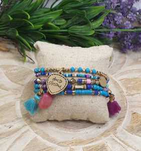 Colorful beaded bracelets with tassels on a textured surface with greenery and flowers in the background
