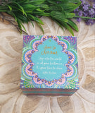 Decorative box with colorful design and text on a wooden surface with greenery