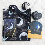  celestial-themed tote bag with notebook, pen, and cards on a textured surface