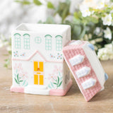 House-shaped container with a lid on a wooden surface with a blurred floral background