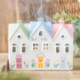 Decorative ceramic house-shaped incense burner with smoke coming out on a wooden surface.