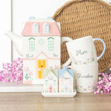 Set of ceramic house-shaped teapots and mugs with decorative designs on a wooden surface.