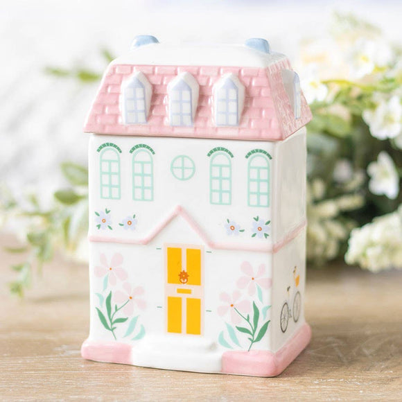 House-shaped container with pink roof and yellow door on a wooden surface with blurred greenery in the background
