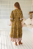 Woman wearing a patterned dress standing in a room with a white couch and decorative items.