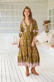 Woman wearing a patterned dress standing in a bright room with white walls and wooden floor.