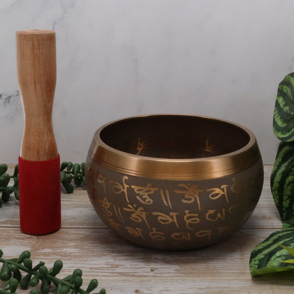 Tibetan singing bowl with wooden striker on a wooden surface with greenery