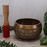 Tibetan singing bowl with wooden striker on a wooden surface with greenery