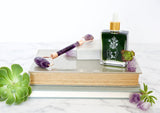 Skincare products including a dropper bottle, roller, and books on a white surface with succulents.