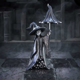 Metallic witch figurine holding an umbrella in a dark, gothic setting