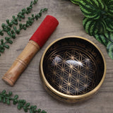 Tibetan singing bowl with floral design, wooden mallet, and green leaves on a wooden surface
