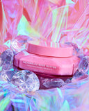 Pink body butter container with 'Bejeweled Body Butter' text on a colorful, gemstone-studded background.