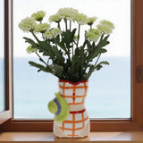 Decorative vase with a patterned design holding white flowers on a windowsill.