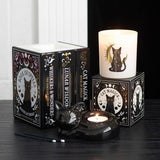 Decorative candles and books with cat-themed design on a dark surface.