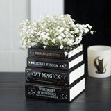 Stack of black books with gold text on a dark surface, topped with white flowers.