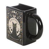 Black mug with a cat illustration and 'Book of Spells' text on a white background