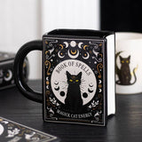 Black mug with a black cat design and text on a wooden surface.