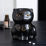 Black cat-shaped ceramic oil burner with gold accents on a dark surface.
