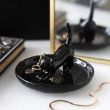 Black cat-shaped trinket dish with jewelry on a white surface