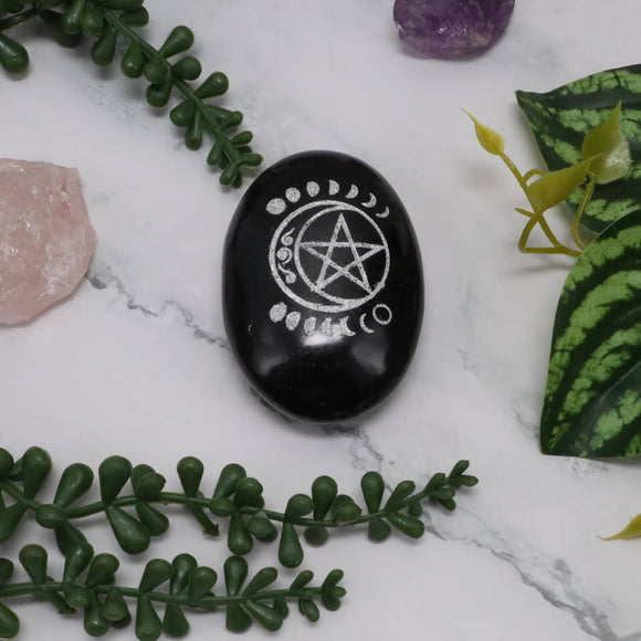 Black stone with a white pentagram symbol on a marble surface with greenery and crystals.