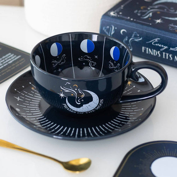 Black ceramic cup and saucer with moon phases design on a white surface.