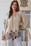 Woman wearing a beige blouse with brown embroidery in a home setting