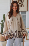 Woman wearing a beige blouse with intricate brown embroidery in a home setting.