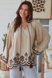 Woman wearing a beige embroidered top in a home setting