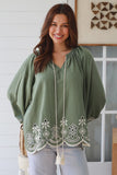 Woman wearing a green top with floral embroidery in a home setting