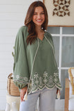 Woman wearing a green embroidered top in a home setting