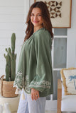 Woman wearing a green top with floral embroidery in a home setting