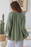 Woman wearing a green blouse with embroidery in a home setting