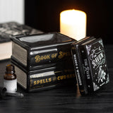 Decorative books titled 'Book of Spells', 'Spells & Curses', and 'The Raven' on a dark surface with a candle in the background.