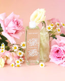 Bottle of 'BOBO WOMEN' floral perfume surrounded by pink roses and daisies on a pink background