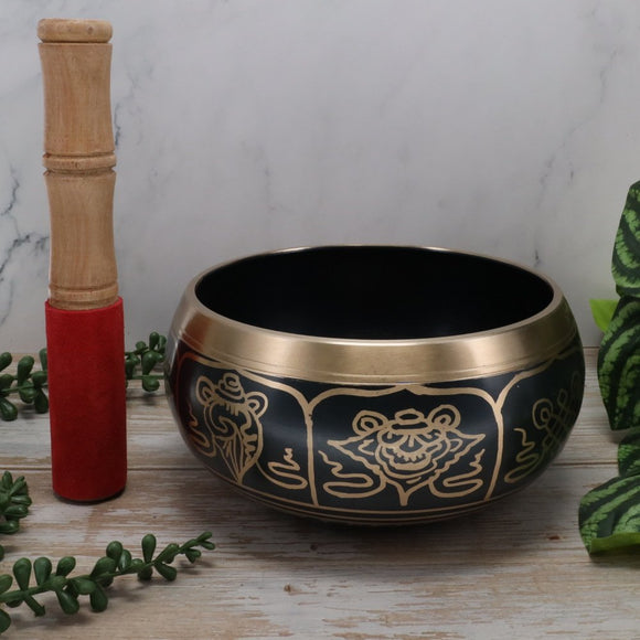 Decorative singing bowl with a wooden beater on a wooden surface with a marble background